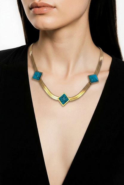 A close-up of a model wearing a gold-toned snake chain necklace with three turquoise blue square inlays, 18k Gold Stainless Steel