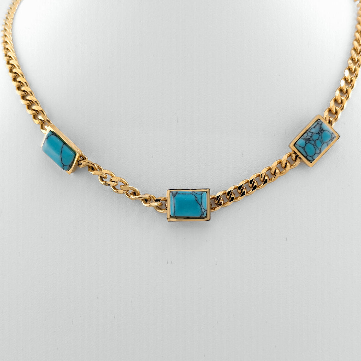 Gold chain necklace with turquoise square stones on a light gray background