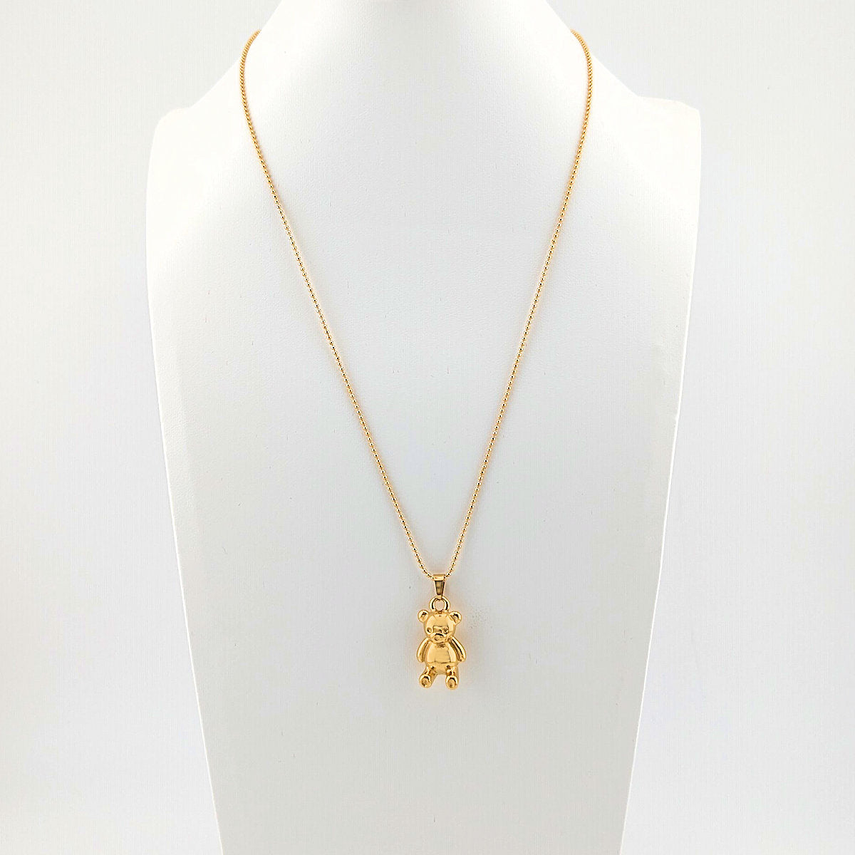 Gold necklace with a teddy bear pendant on a mannequin bust against a white background