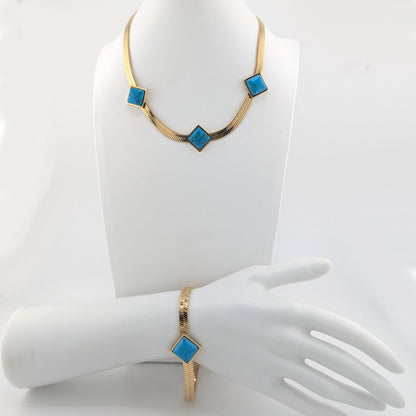 Gold-tone jewelry set featuring a necklace and matching bracelet with a textured snake-skin style band and a central turquoise blue square bezel-set stone, displayed on a white mannequin hand and bust.