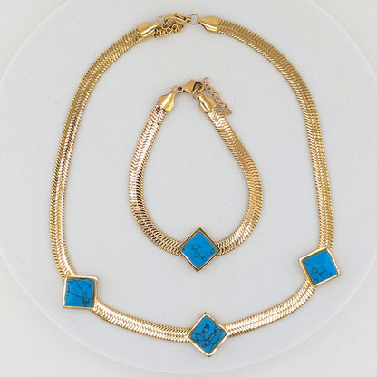 Gold snake chain necklace and matching bracelet set, each decorated with three square turquoise blue inlay accents, displayed on a white circular surface.