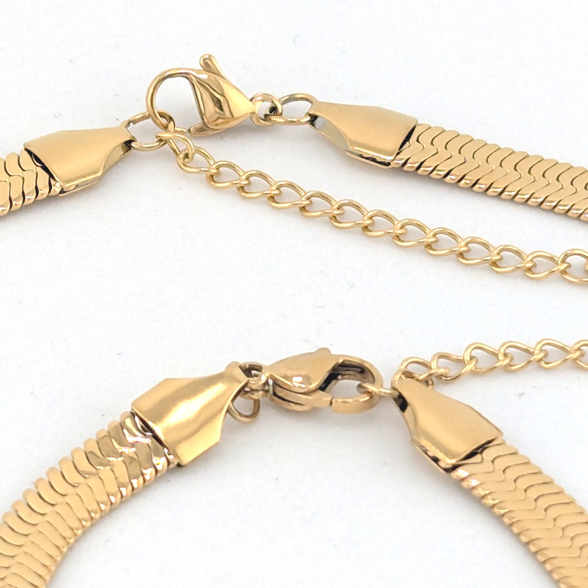 Close-up of a gold-tone chain necklace with a textured snake-link style band and lobster clasp on a white background.