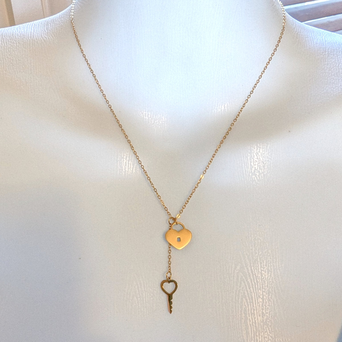 A delicate gold necklace featuring a small heart-shaped pendant with a keyhole cutout and a dangling key charm.
