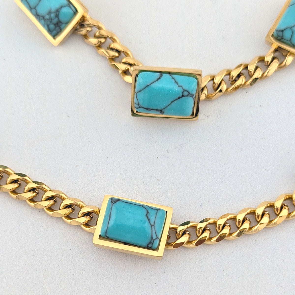 Gold chain necklace with turquoise stone pendants on a light gray background