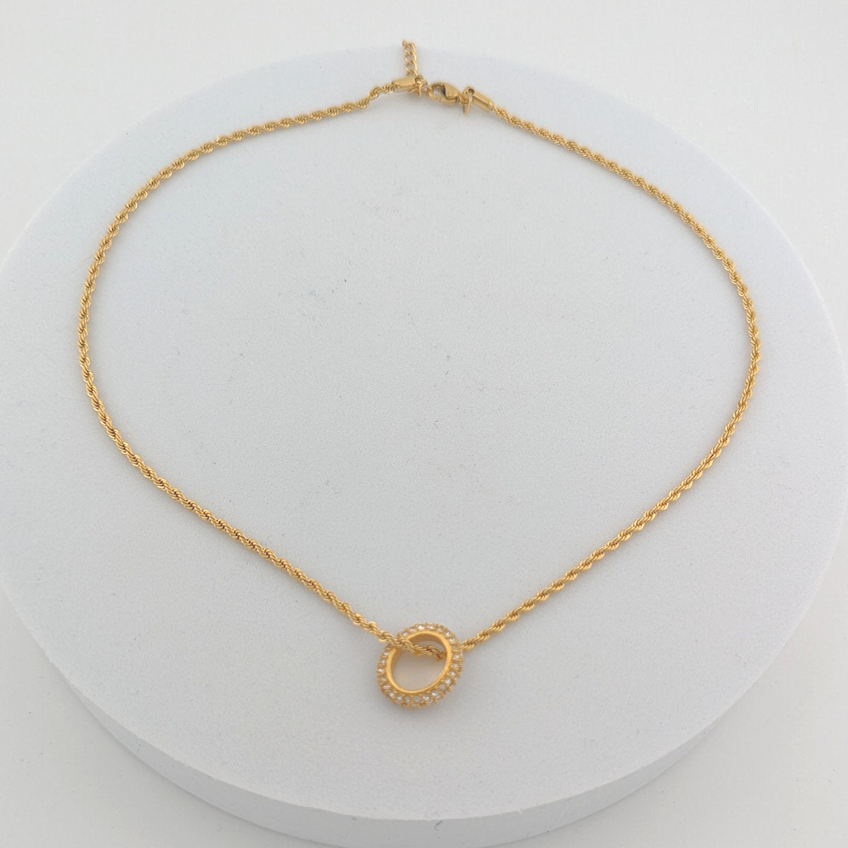 Gold necklace with a small circular pendant on a white background
