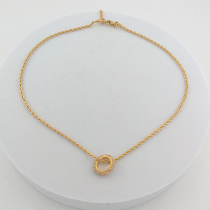 Gold necklace with a small circular pendant on a white background