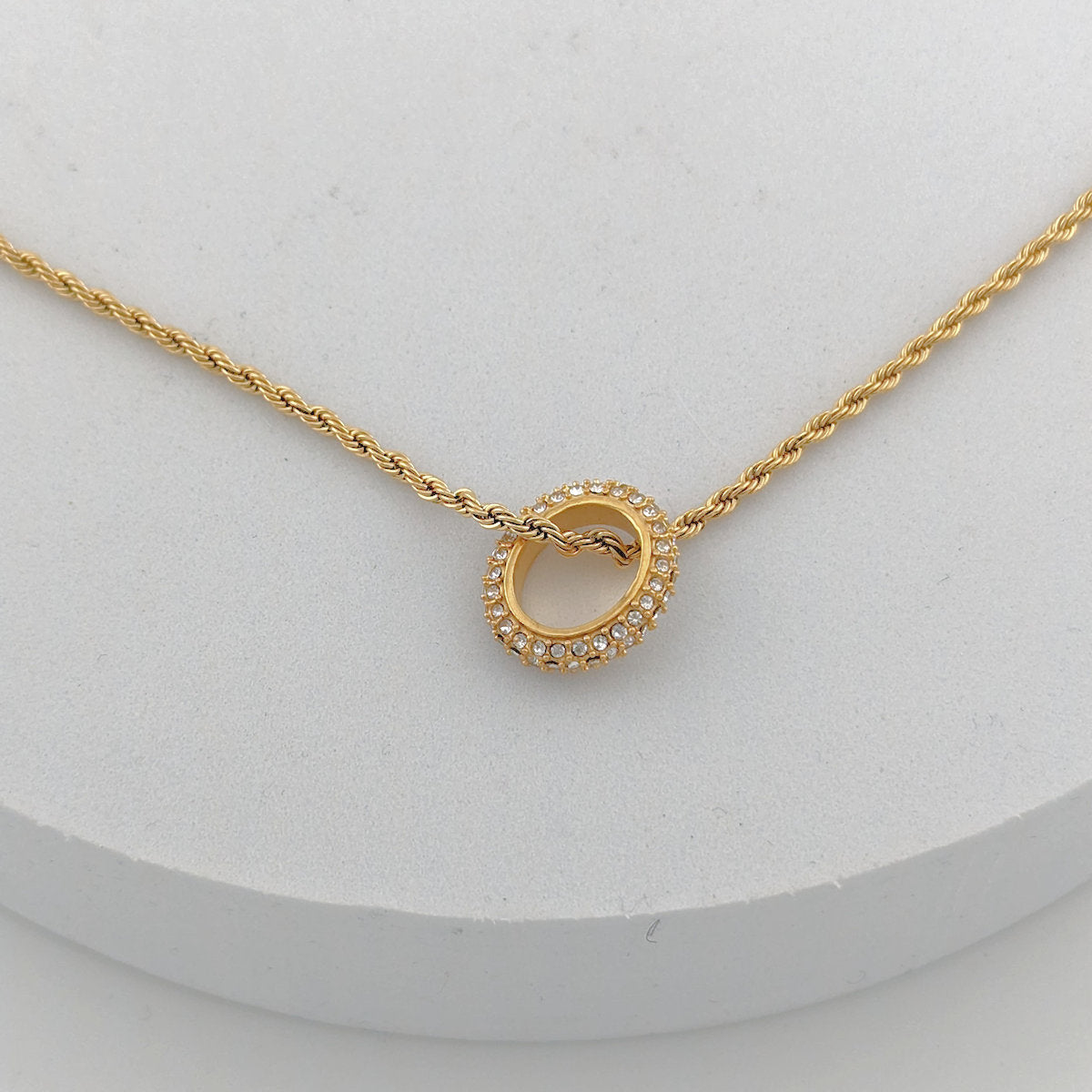 Gold necklace with a circular pendant on a white background