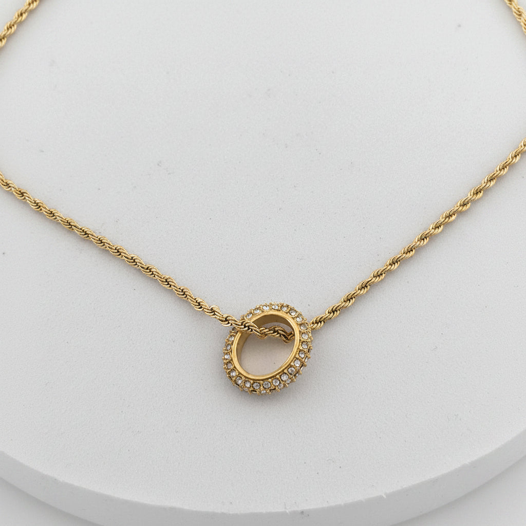 Gold necklace with a circular pendant on a light gray background