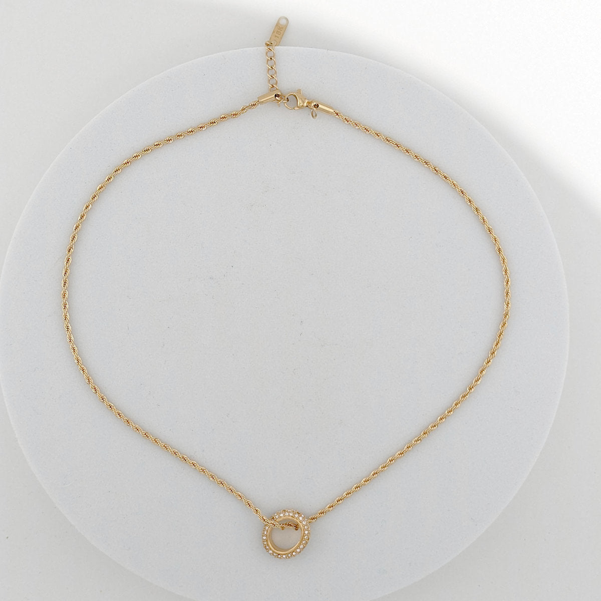 Gold necklace with a small round pendant on a white background