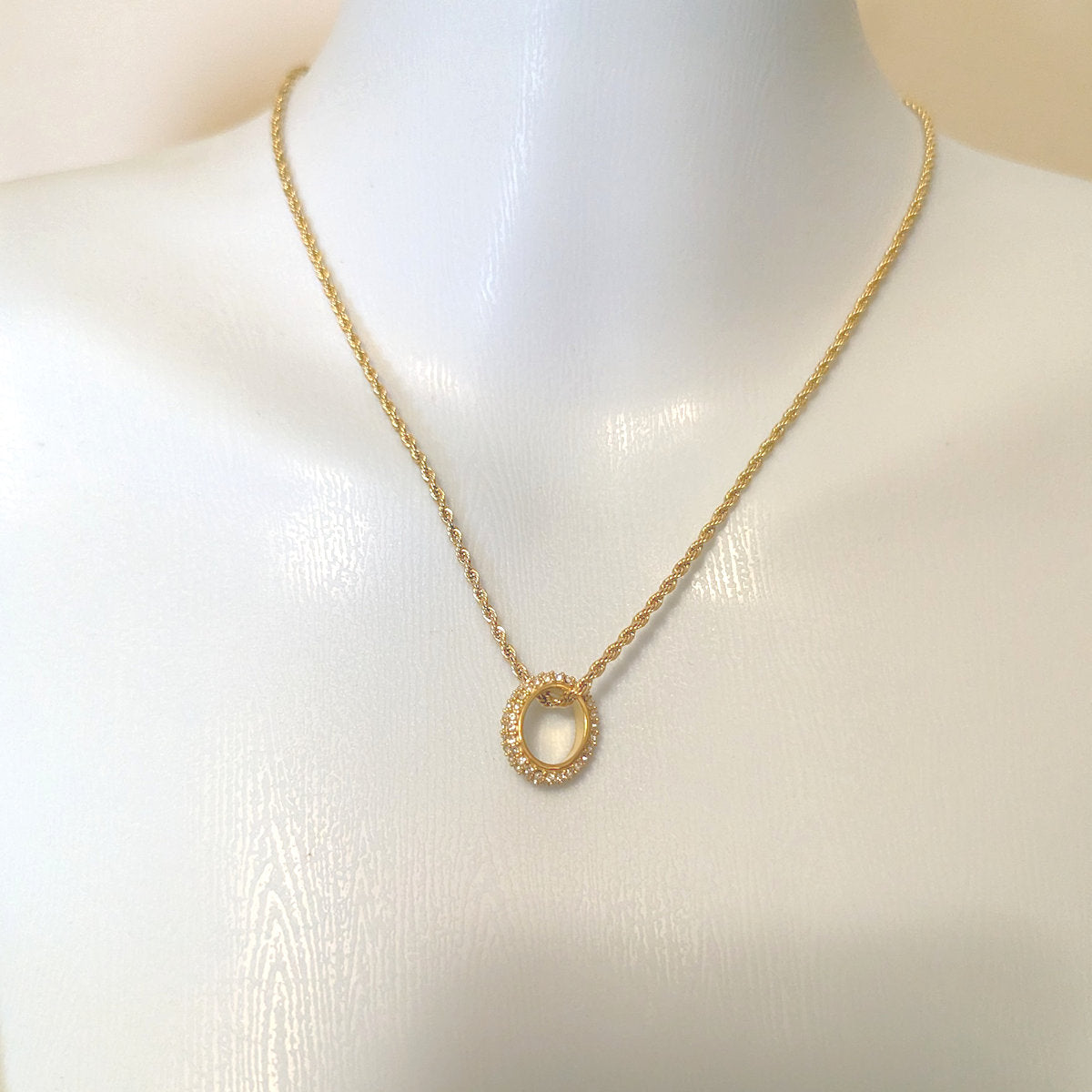 Gold necklace with a circular pendant on a mannequin.