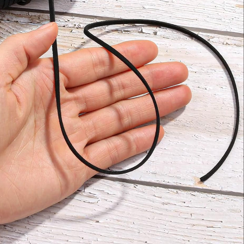 Black elastic cord with a spool and a hand holding a loop of cord on a wooden surface.
